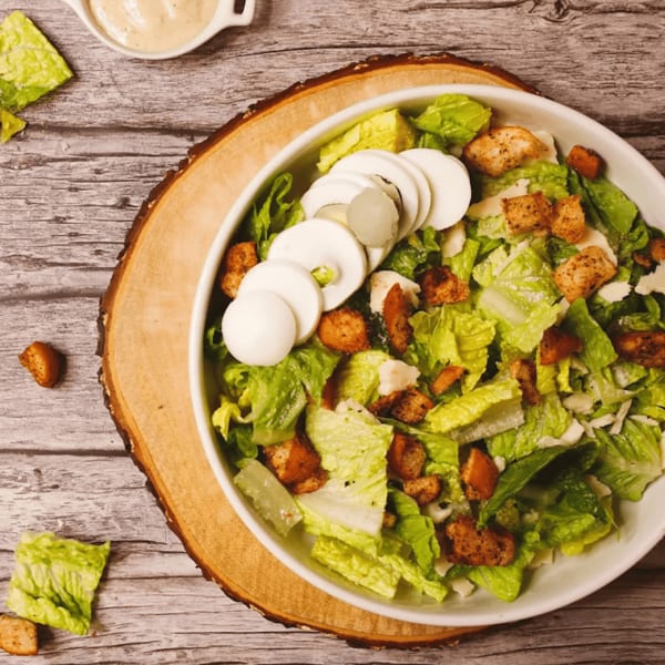Caesar salad with lettuce, croutons, sliced hard-boiled eggs, and dressing on a wooden board.