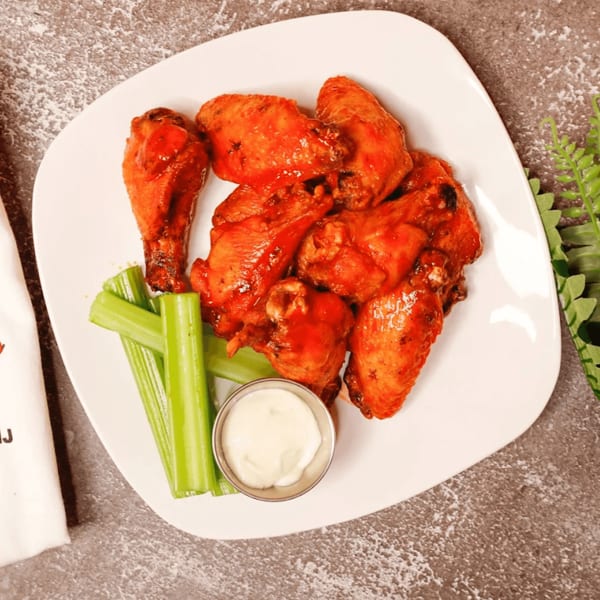 A white plate of buffalo wings with celery sticks and a side of ranch dressing.
