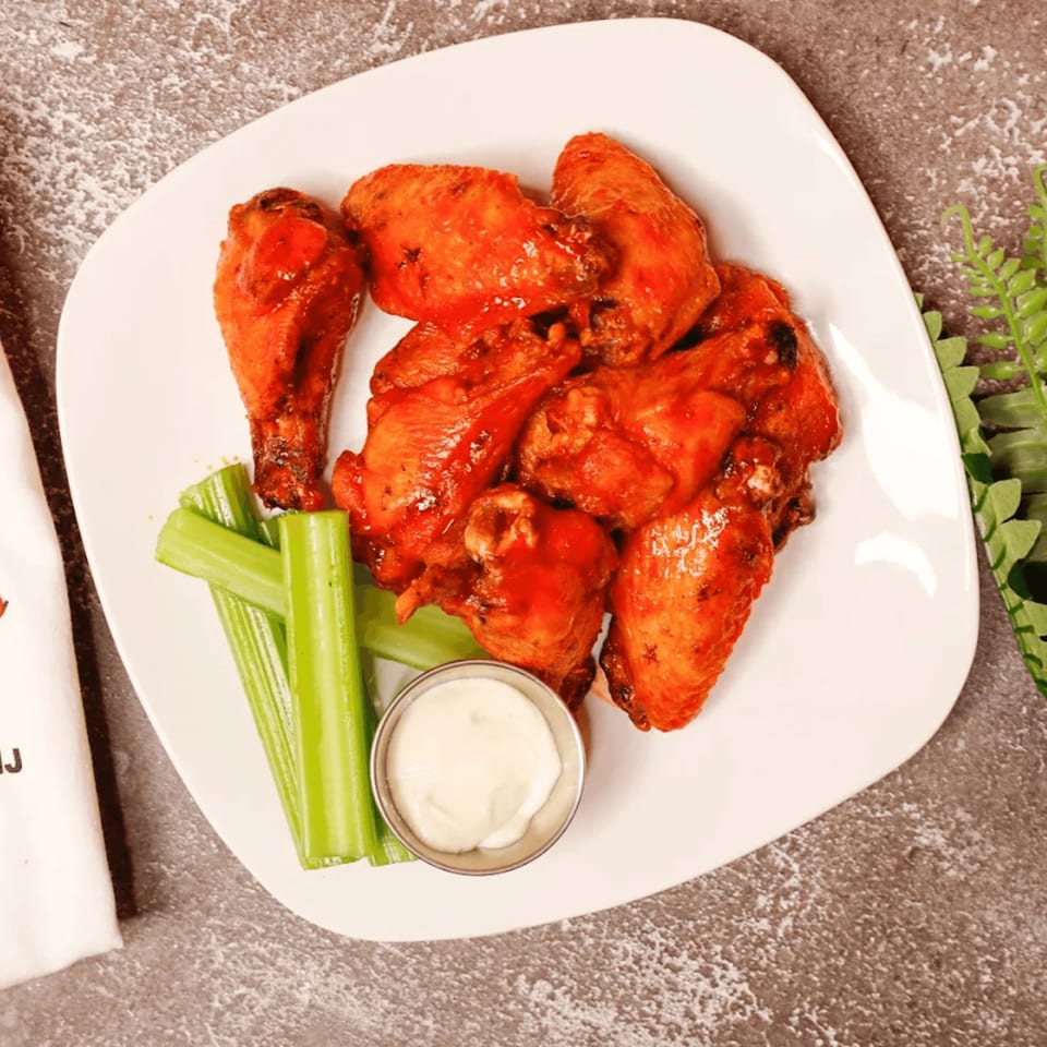A white plate of buffalo wings with celery sticks and a side of ranch dressing.