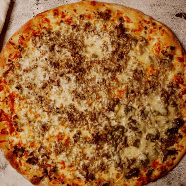 Overhead view of a whole pizza with a golden crust, melted cheese, and ground meat toppings.