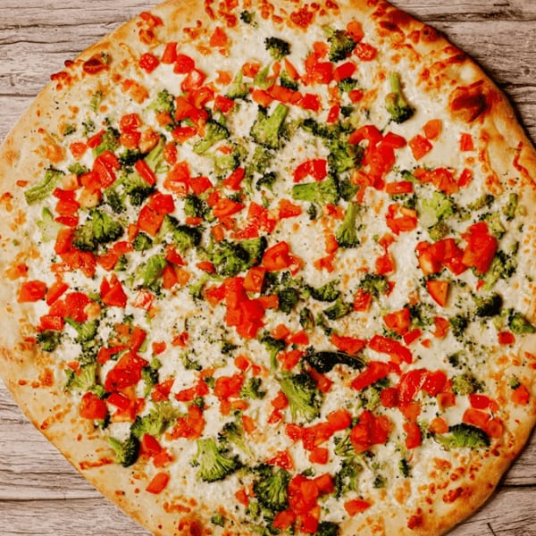 A white pizza with a golden crust, topped with melted cheese, diced tomatoes, and broccoli florets.
